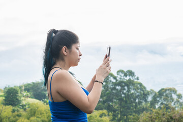 young latina woman taking a picture of a landscape in the beautiful colombian mountains. influencer girl creating content for her social networks, while hiking. technology concept