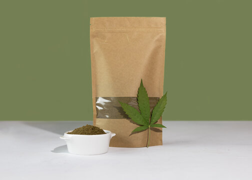 Hemp flour in a brown kraft paper doypack bags with groceries front view on a green background. Packs with windows for weight products.