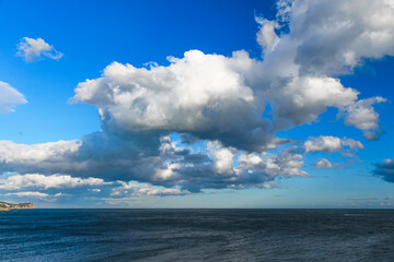 Naklejka na ściany i meble A seascape with beautiful big white clouds in a blue sky. Calm sea water.