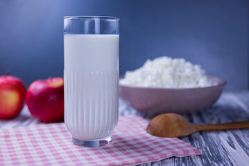 dairy product cottage cheese in a plate with a glass of milk and apples on a wooden background