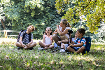Group of children sitting on grass in the forest with their teacher.They learn about nature and wildlife. 