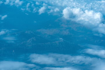 Fototapeta na wymiar view of the earth below while flying above the clouds, mountainous terrain through atmospheric haze, view from above