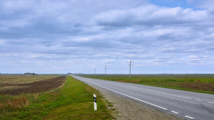 Fototapeta na wymiar View of the asphalt road going beyond the horizon, passing by the fields. Highway with two-way traffic lanes.