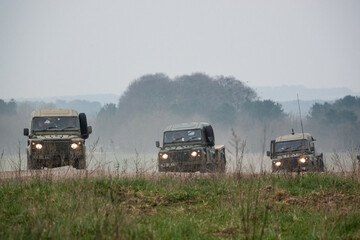 a small convoy British Army Land Rover Defender Wolf medium utility vehicles in action on a military exercise - Powered by Adobe