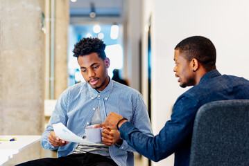 Two young black men working in an office, consulting reports and chatting about their business plan. people working in an office