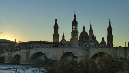 Obraz premium Panoramic view of the stone bridge and the Basilica del Pilar at sunset in Zaragoza, Spain.