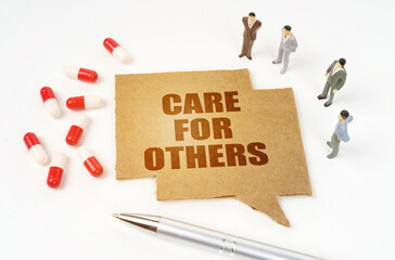On a white surface are pills, a pen, figurines of people, a sign with the inscription - CARE FOR OTHERS