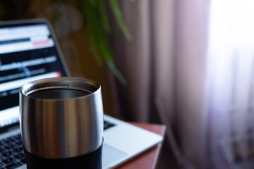 metal thermo mug with a hot drink on the background of a laptop