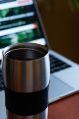 metal thermo mug with a hot drink on the background of a laptop