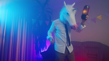 A young man in a unicorn mask is dancing with a music column in his hands. Multicolored lighting....