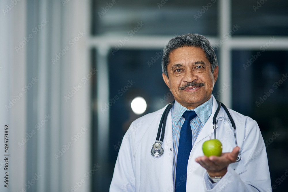 Wall mural I recommend at least one of these a day. Portrait of a mature doctor holding a green apple in a hospital.