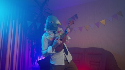 A young man in a pigeon mask plays the ukulele. Multicolored lighting. Masquerade