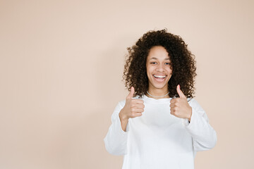 Portrait of cheerful african american girl two hands show thumb up toothy smile isolated on brown...