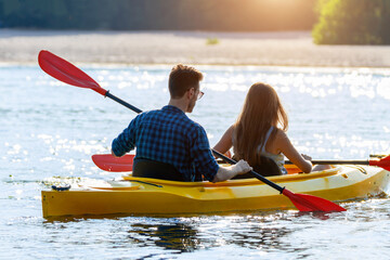 Confident young caucasian couple kayaking on river together with sunset in the backgrounds. Having fun in leisure activity. Romantic and happy woman and man on the kayak boat. Sport, relations concept