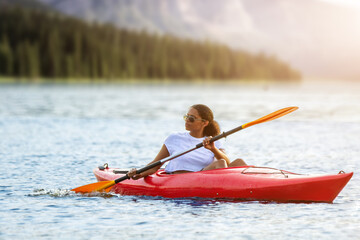 Confident young woman kayaking on river alone with mountains sunset in the backgrounds. Having fun in leisure activity. HÑƒalthy active girl spend weekend on the kayak boat. Sport, relations concept