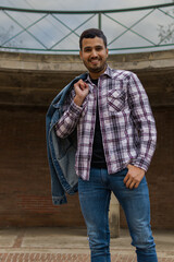 Three quarter length image of a handsome Hispanic man carrying his jacket over his shoulder while is standing in a viewpoint plaza and looking at the camera smiling