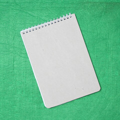 White and gray notepad sheet with spiral against the background of green fabric. Concept of analysis, study, attentive work. Stock photo with empty place for your text and design.