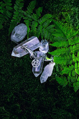 quartz crystals and amulet pentacle with fern leaves on natural dark forest background. gemstones...