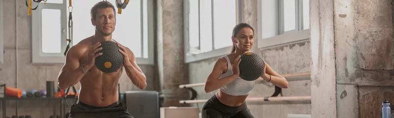 Tuinposter Concentrated sporty man and woman with athletic bodies working out with exercise balls in gym club © Yaroslav Astakhov