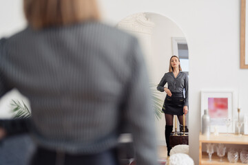 Self-confident Woman looking at her reflection into the mirror indoors. Beautiful interior design