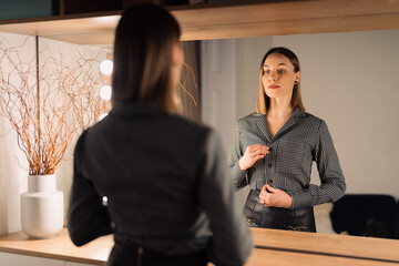 Self-confident Woman looking at her reflection into the mirror indoors. Beautiful interior design