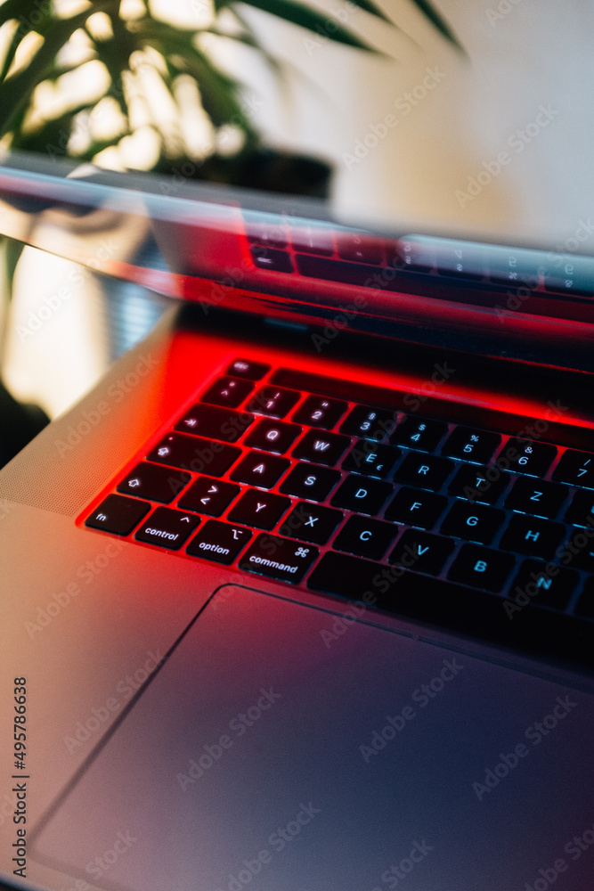 Poster vertical shot of a half-opened laptop keyboard with under the red light from the screen