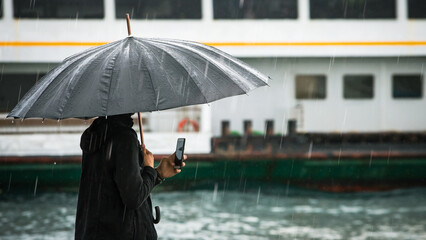 Male traveler holding his smartphone by the sea on a rainy day