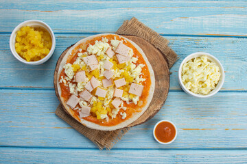 Artisan pizza before baking, with cheese, ham, pineapple, pomodoro sauce, accompanied by flavors