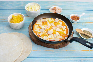 Artisan pizza before baking, with cheese, ham, pineapple, pomodoro sauce, accompanied by flavors