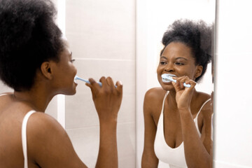 Portrait happy black African American girl brushing teeth in the bathroom. Morning routine with...
