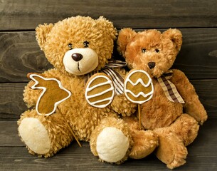 Decorative postcard on a wooden background, brown fluffy teddy bears sit in their paws with Easter cookies, a rabbit and eggs.  Holiday atmosphere.  The concept of a bright Easter holiday.