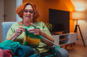 Mature woman holding knitting needles and knitting at home.