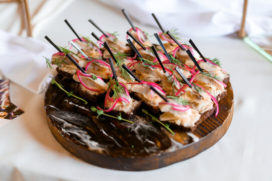 Above View Of Festive Appetizer On Wooden Tableware, Which Includes Toast Rounds, Fish And Decorated By Red Onion And Micro Greens, Located On Wedding Buffet