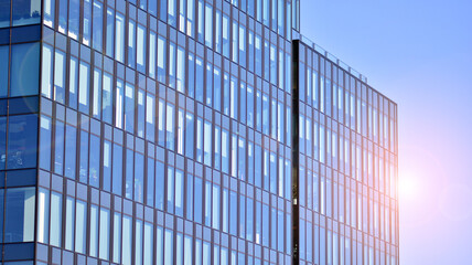 Glass building with transparent facade of the building and blue sky. Structural glass wall reflecting blue sky. Abstract modern architecture fragment. Contemporary architectural background.