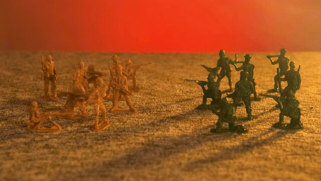 Plastic toy soldiers stand opposite each other on a red background. The concept of military confrontation