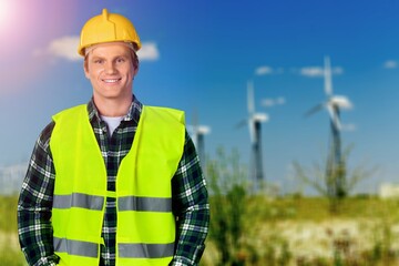 Beautiful man in white helmet working with digital tablet at energy farm. Male inspector controlling functioning of wind turbines outdoors.