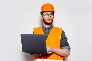 Studio portrait of young construction worker on white, with laptop in hands.