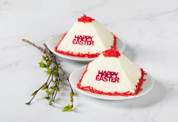 Festive dessert. Cottage cheese creamy Easter, decorated with red confectionery sprinkles, on a plate with spring birch twigs. Light background