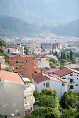 Houses with tiled roofs against the backdrop of mountains for publication, poster, calendar, post, wallpaper, postcard, banner, cover, website. City view of Budva on a sunny day for design or text.