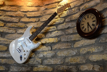 Electric guitar and a clock hanging on the brick wall