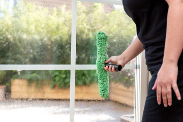 Person washing a window from the inside. Outside there is a green garden