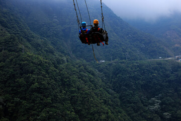 Obraz premium Two tourist are relaxing in a giant swing with a mountain and forest in the background: a famous tourist attraction which swings over a raving or canyon in Ecuador