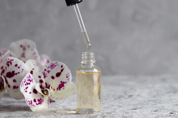 Serum oil is dripping from dropper. Bottle of cosmetic essential oil with dropper and orchid...