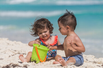 Two young latin babies playing on the sand at a caribbean beach