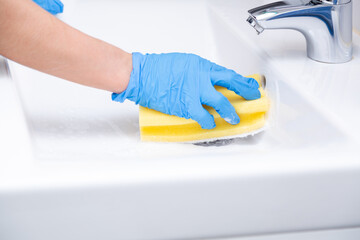 Hand with blue glove cleaning a sink with a yellow sponge