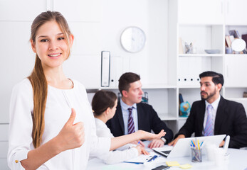 Fototapeta premium Confident smiling businesswoman with team in office showing thumbs up