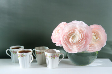 Three pale pink ranunculus in a transparent round vase on the white windowsill. Copy space. Place for text
