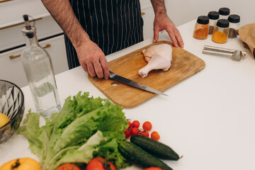 Products for cooking on the kitchen table. A man cuts a chicken on a board