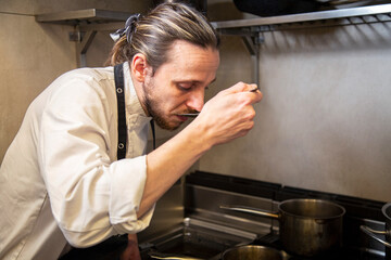 chef prueba cuchara salsa en inetrior cocina restaurante close-up
