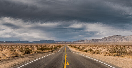 Obraz na płótnie Canvas Panorama of desert highway in leading to mountains under a dark stormy sky; concepts of adventure, uncertainty, future, travel 